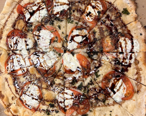 A circular pizza topped with sliced tomatoes, dollops of cheese, and drizzled with balsamic glaze, cut into slices.