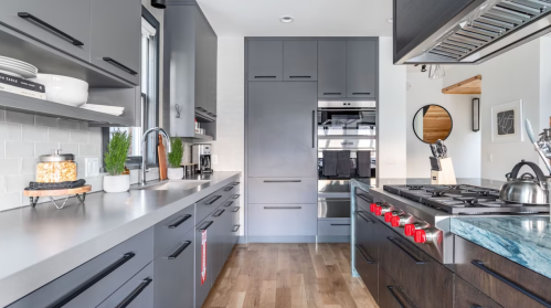Modern kitchen with sleek gray cabinets, stainless steel appliances, and a large island featuring a gas stove and wooden flooring.
