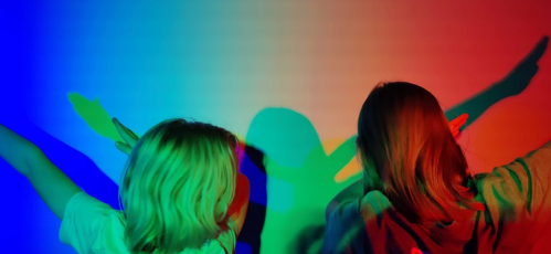 Two children create colorful shadows on a wall, with vibrant blue, green, and red lighting.