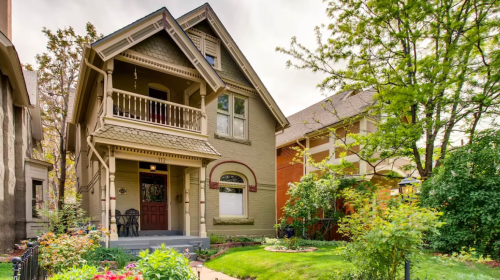A charming two-story house with a porch, surrounded by greenery and colorful flowers in the front yard.