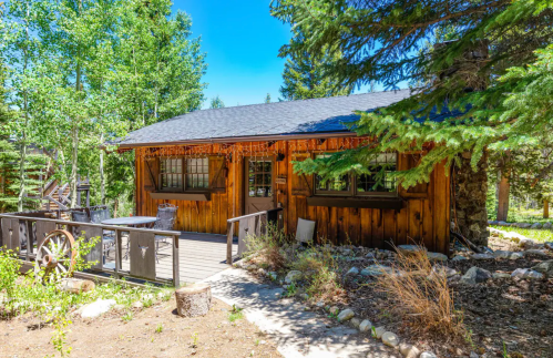 A rustic wooden cabin surrounded by trees, featuring a deck and outdoor seating in a serene natural setting.