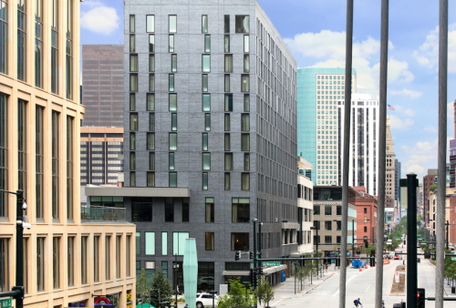 Modern buildings line a city street, showcasing a mix of architectural styles against a clear blue sky.