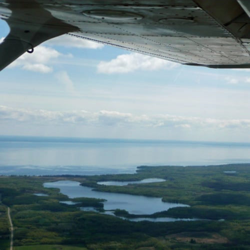Aerial view of lakes and lush green land under a clear sky, with a plane wing in the corner of the image.