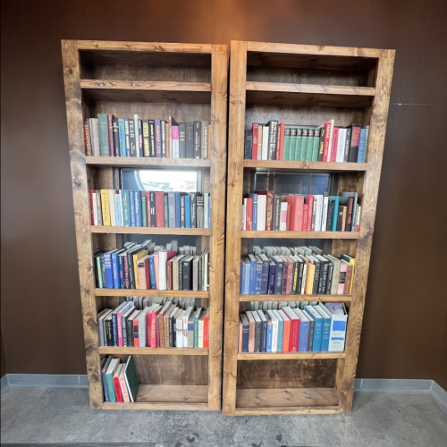 A wooden bookshelf filled with various books, arranged in two sections against a brown wall.