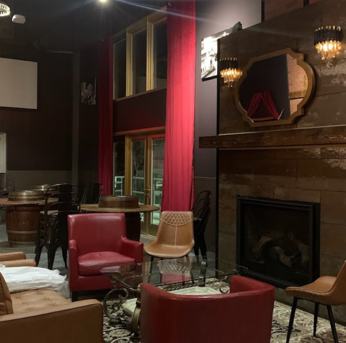 Cozy interior of a lounge with red curtains, a fireplace, and stylish seating around a glass table.
