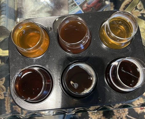 A tray with six small glasses filled with various colored liquids, arranged in two rows.