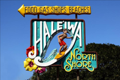 Colorful sign for Haleiwa, North Shore, featuring a surfer and flowers, with directions to food, gas, shops, and beaches.