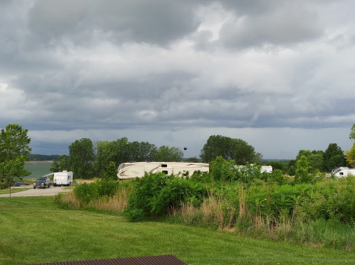 A cloudy sky over a campground with RVs, surrounded by greenery and a view of a lake in the distance.