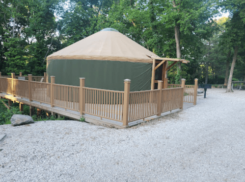 A yurt on a wooden deck surrounded by trees, with a gravel path leading to it.