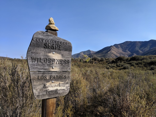 Wooden sign for Sespe Wilderness in Los Padres National Forest, with mountains and clear blue sky in the background.