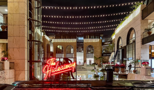 A vibrant neon sign reading "The Hideaway" illuminated in a stylish courtyard with string lights above.