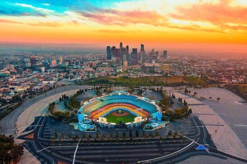 Aerial view of a stadium at sunset, with a city skyline in the background and colorful clouds in the sky.