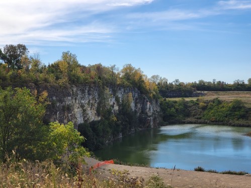 A serene landscape featuring a calm lake surrounded by rocky cliffs and autumn-colored trees under a clear blue sky.