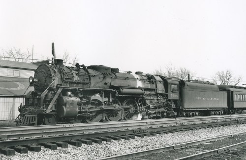 A vintage steam locomotive with "New York Central" on the side, parked on tracks with trees in the background.