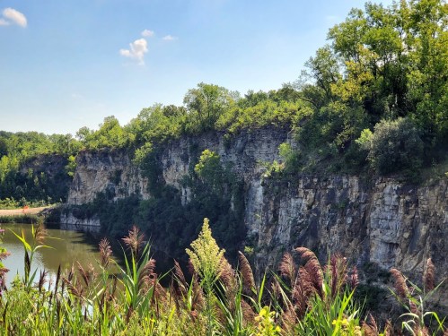 A scenic view of a rocky cliff surrounded by lush greenery and a calm body of water under a clear blue sky.