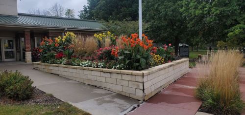 A landscaped flower bed with colorful blooms and tall grasses near a building entrance on a cloudy day.
