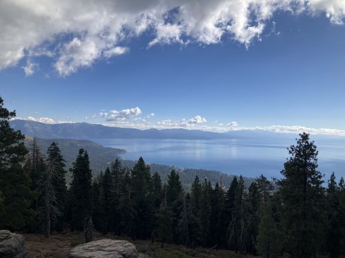 A scenic view of a lake surrounded by mountains and trees under a partly cloudy sky.