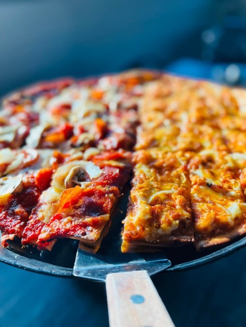 A close-up of a pizza pan with two types of pizza: one with pepperoni and vegetables, the other with cheese and mushrooms.