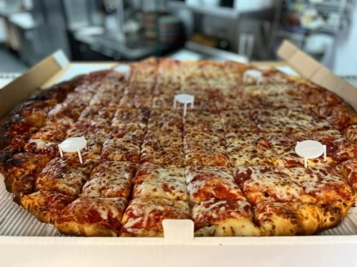 A large pizza with melted cheese and pepperoni, cut into slices and placed in a pizza box with white pizza savers.
