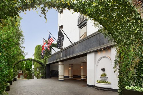 Entrance of a hotel with greenery, flags, and a fountain, creating a welcoming atmosphere.