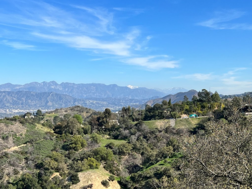 A scenic view of rolling hills and mountains under a clear blue sky, with distant snow-capped peaks.