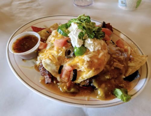 A plate of nachos topped with cheese, eggs, olives, tomatoes, and green onions, served with a side of salsa.