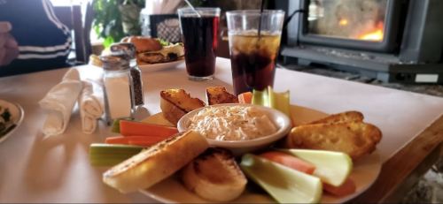 A plate of celery, carrots, and toasted bread with a creamy dip, alongside two glasses of iced drinks.