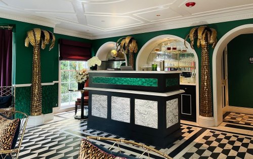A stylish interior featuring a reception desk, green walls, palm tree decor, and a patterned floor.