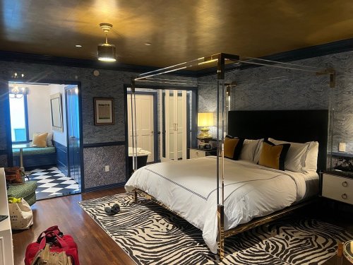 A stylish hotel room featuring a four-poster bed, zebra print rug, and a cozy seating area in the background.