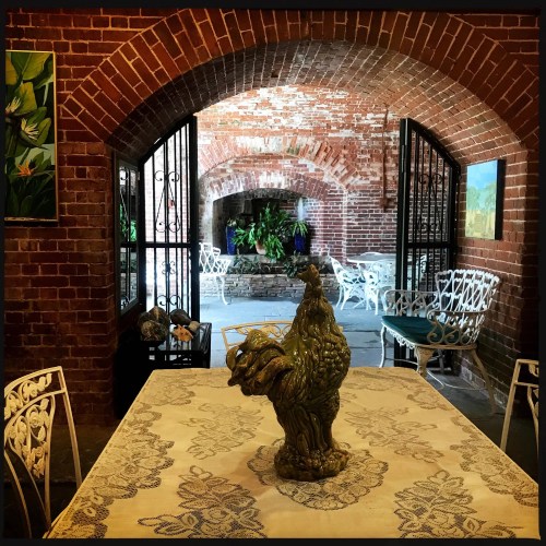 A rustic dining area with a decorative chicken centerpiece, brick arches, and white wrought iron furniture.