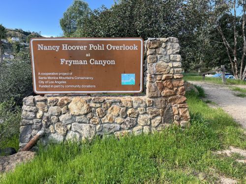 Sign for Nancy Hoover Pohl Overlook at Fryman Canyon, surrounded by greenery and trees.