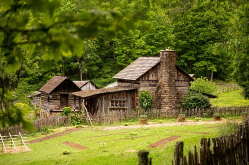 A rustic wooden farmhouse surrounded by greenery and a wooden fence, set in a peaceful rural landscape.