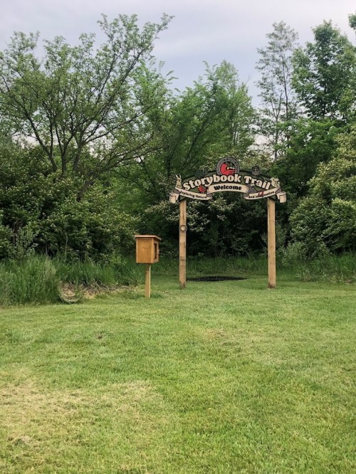 A wooden archway with a sign reading "Storybook Trail" welcomes visitors to a lush, green outdoor area.