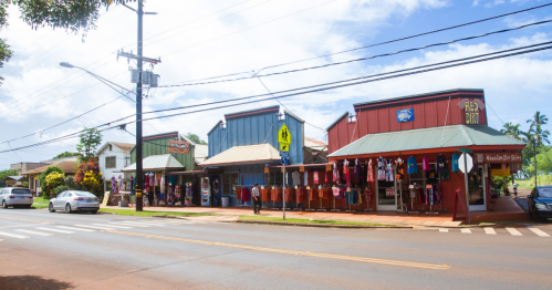 Colorful storefronts line a street, with clothing displayed outside and a clear blue sky above.