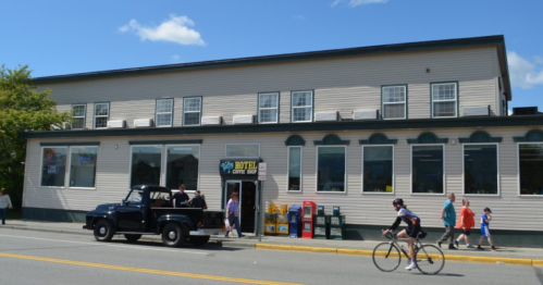 A two-story hotel with a vintage truck parked outside, people walking by, and bright blue skies above.