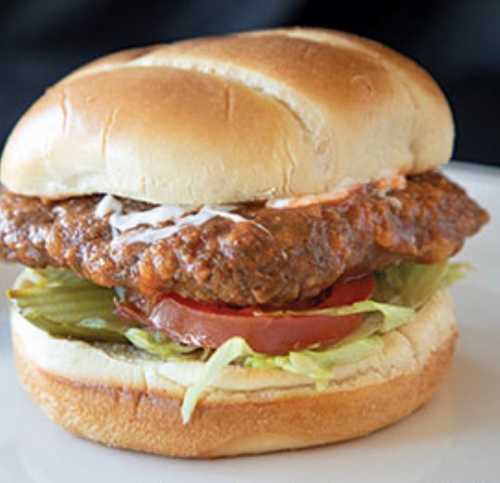 A crispy chicken sandwich with lettuce, tomato, and sauce on a soft bun, served on a white plate.