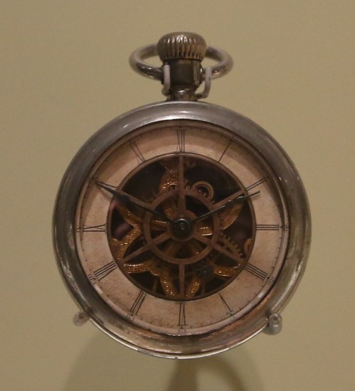 A vintage pocket watch with a visible intricate gear mechanism and Roman numerals on the face.