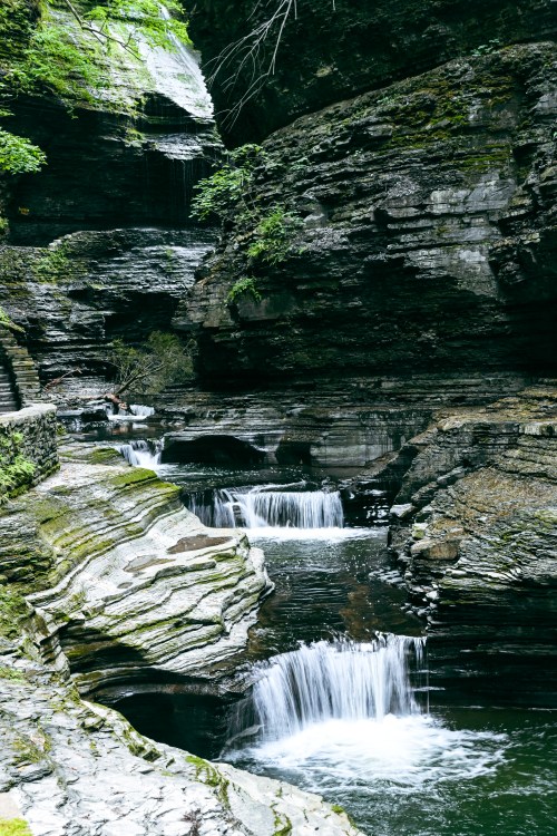 A serene landscape featuring cascading waterfalls and smooth, moss-covered rocks in a lush, green gorge.