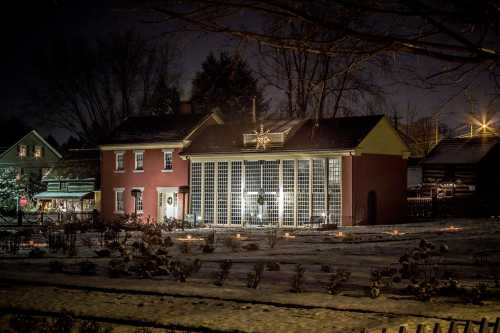 A beautifully lit brick house at night, surrounded by snow and festive decorations, with a star on the roof.