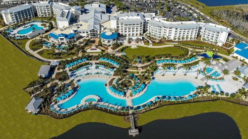 Aerial view of a resort featuring multiple pools, cabanas, and landscaped grounds near a lake.