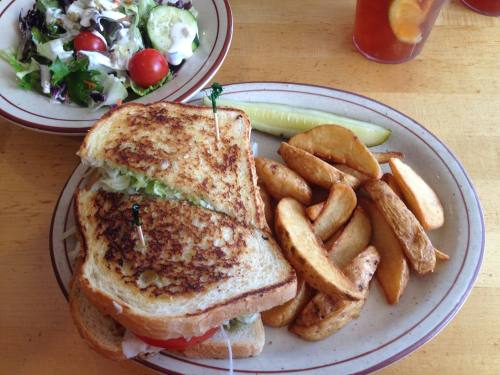 A toasted sandwich with lettuce and tomato, served with potato wedges and a side salad.