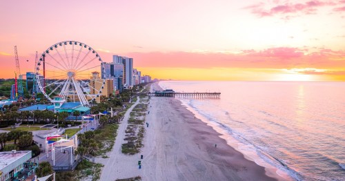A scenic view of a beach at sunset, featuring a ferris wheel and a pier along the coastline.
