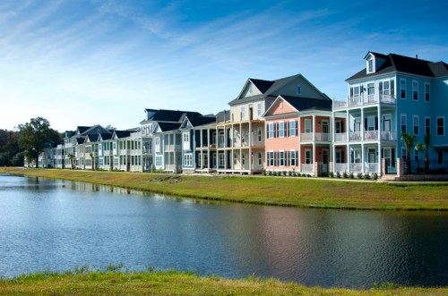 Colorful waterfront houses line a serene lake under a clear blue sky. Green grass frames the scene.