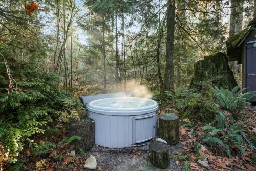 A hot tub surrounded by lush greenery and trees, with steam rising in a serene forest setting.