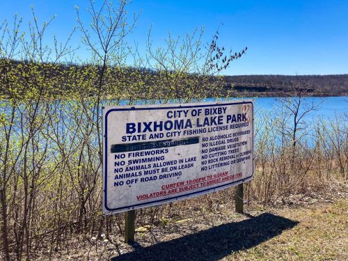 Sign at Bixhoma Lake Park listing rules and regulations, with a clear blue sky and water in the background.