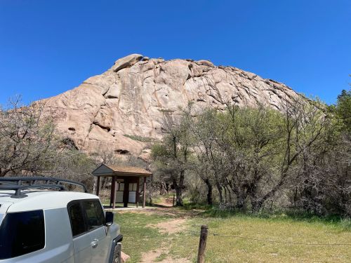A rocky hill under a clear blue sky, with a parked vehicle and a small shelter in the foreground.