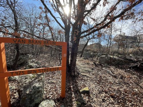 A sign reading "Van Bran Brun T 975 Ben Streeter" in a wooded area with bare trees and rocky terrain.