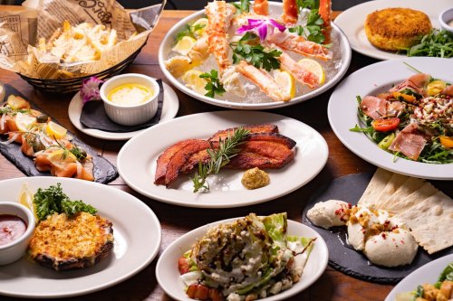 A variety of gourmet dishes including seafood, salads, and appetizers arranged on a wooden table.