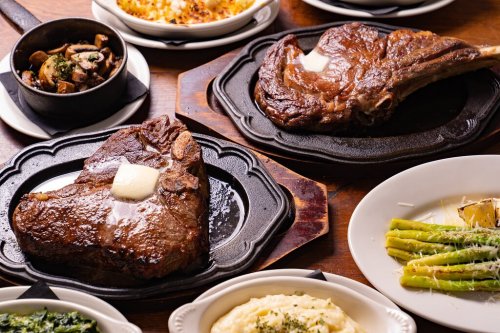 A table spread featuring two large steaks with butter, sides of mushrooms, asparagus, and mashed potatoes.
