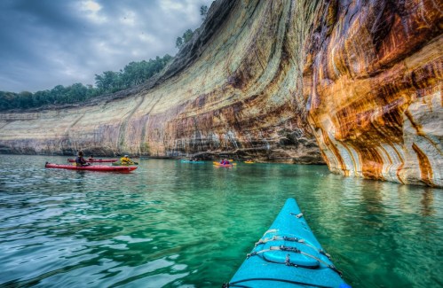 A kayak in clear water near colorful rock formations, with other kayakers exploring the scenic coastline.